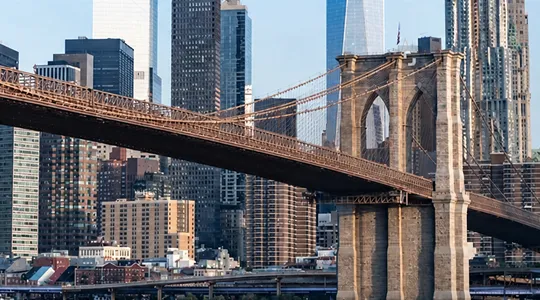 Brooklyn Bridge with suspension cables and New York City skyline in daylight.