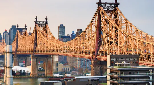 View of a large steel suspension bridge with city skyline in the background.