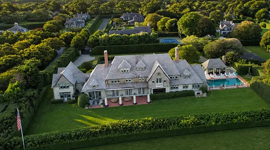 Aerial view of a large estate with a mansion, swimming pool, tennis court, and surrounding greenery.