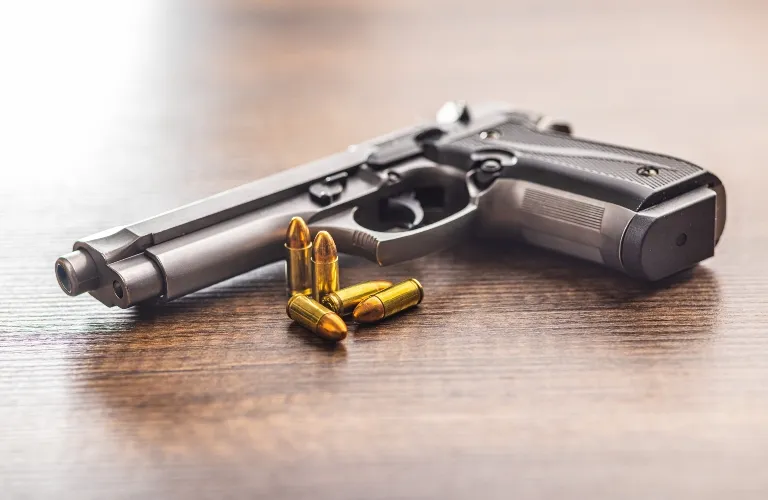 Black semi-automatic handgun with five brass bullets on a wooden surface.
